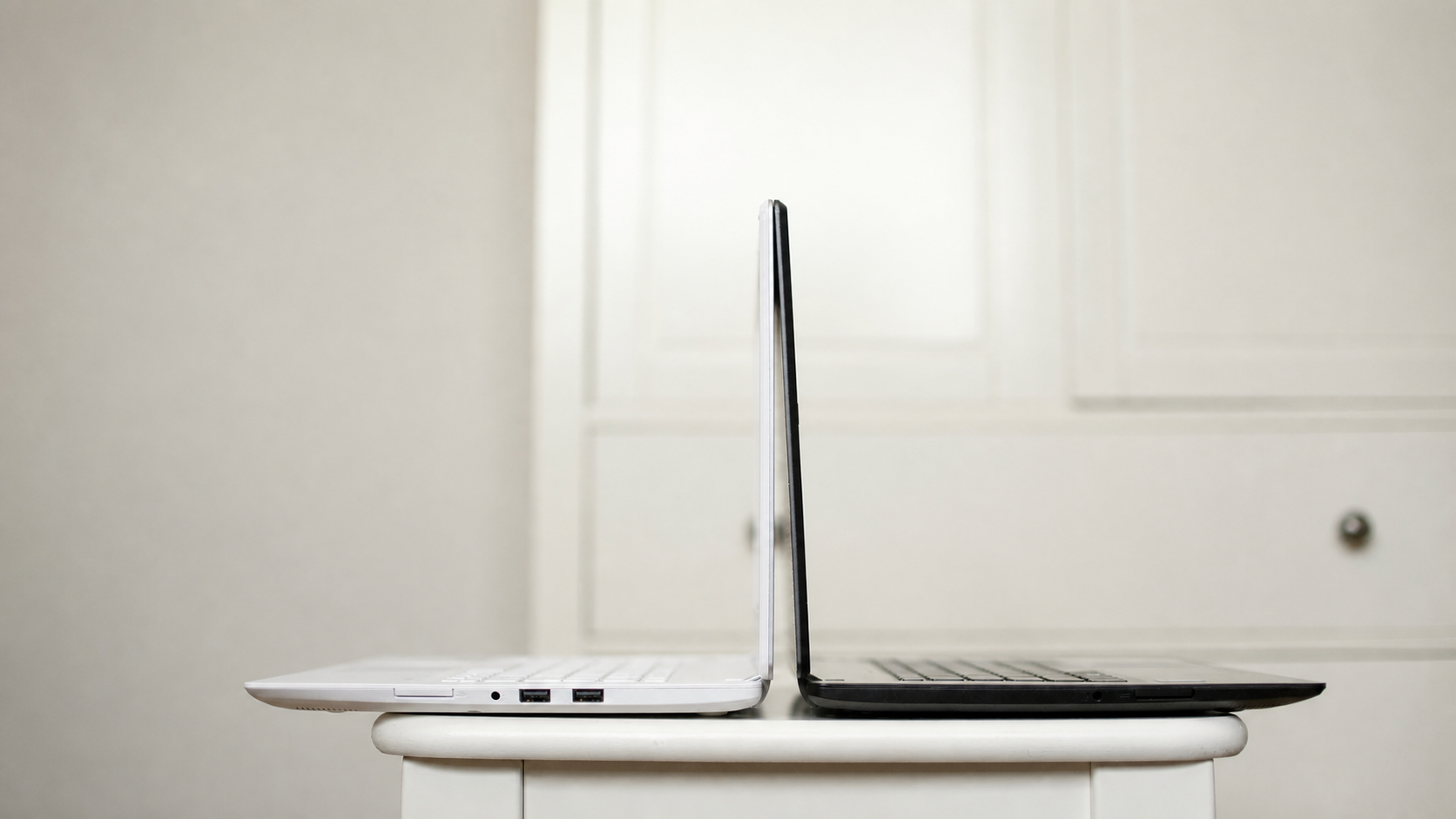 Two open laptops shown edge-on and placed back-to-back on a white table.