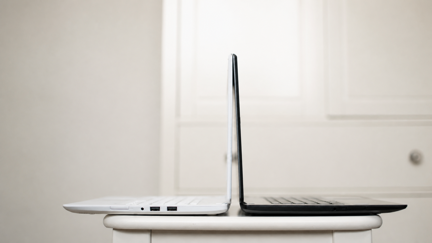 Two open laptops positioned back-to-back on a small white table.